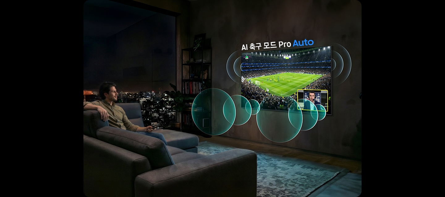 남성이 소파에 앉아서 벽에 설치된 TV를 보고 있습니다. TV 화면에는 축구 경기가 보여지고 있습니다.